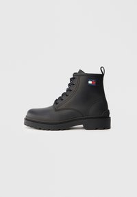 Ghete negre până la gleznă din piele netedă, cu vârf rotund, talpă din cauciuc rezistentă și un patch cu logo pe lateral. Design cu șireturi.