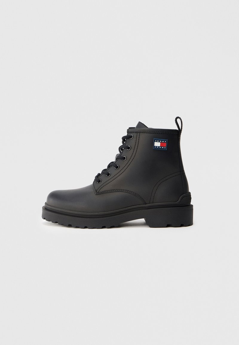 Ghete negre până la gleznă din piele netedă, cu vârf rotund, talpă din cauciuc rezistentă și un patch cu logo pe lateral. Design cu șireturi.