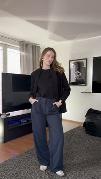 Čierny blejzer cez čierne tričko, skombinovaný s tmavomodrými nohavicami s vysokým pásom. Svetlé tenisky a veľké zlaté náušnice dopĺňajú vzhľad.