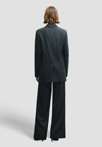 Zwart krijtstreeppak met een lange, getailleerde blazer en broek met wijde pijpen, met nadruk op textuurrijk stof en een gestructureerd ontwerp.