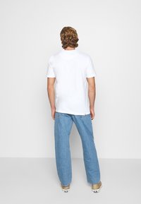 T-shirt blanc à manches courtes, coupe décontractée. Associé à un pantalon en denim bleu clair, avec un design relax et des jambes droites.