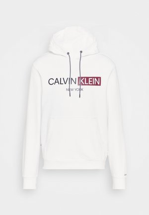 Sudadera blanca con capucha, bolsillo frontal tipo canguro, cordones en blanco y negro, y logo de texto "CALVIN KLEIN NEW YORK" en negro y rojo.