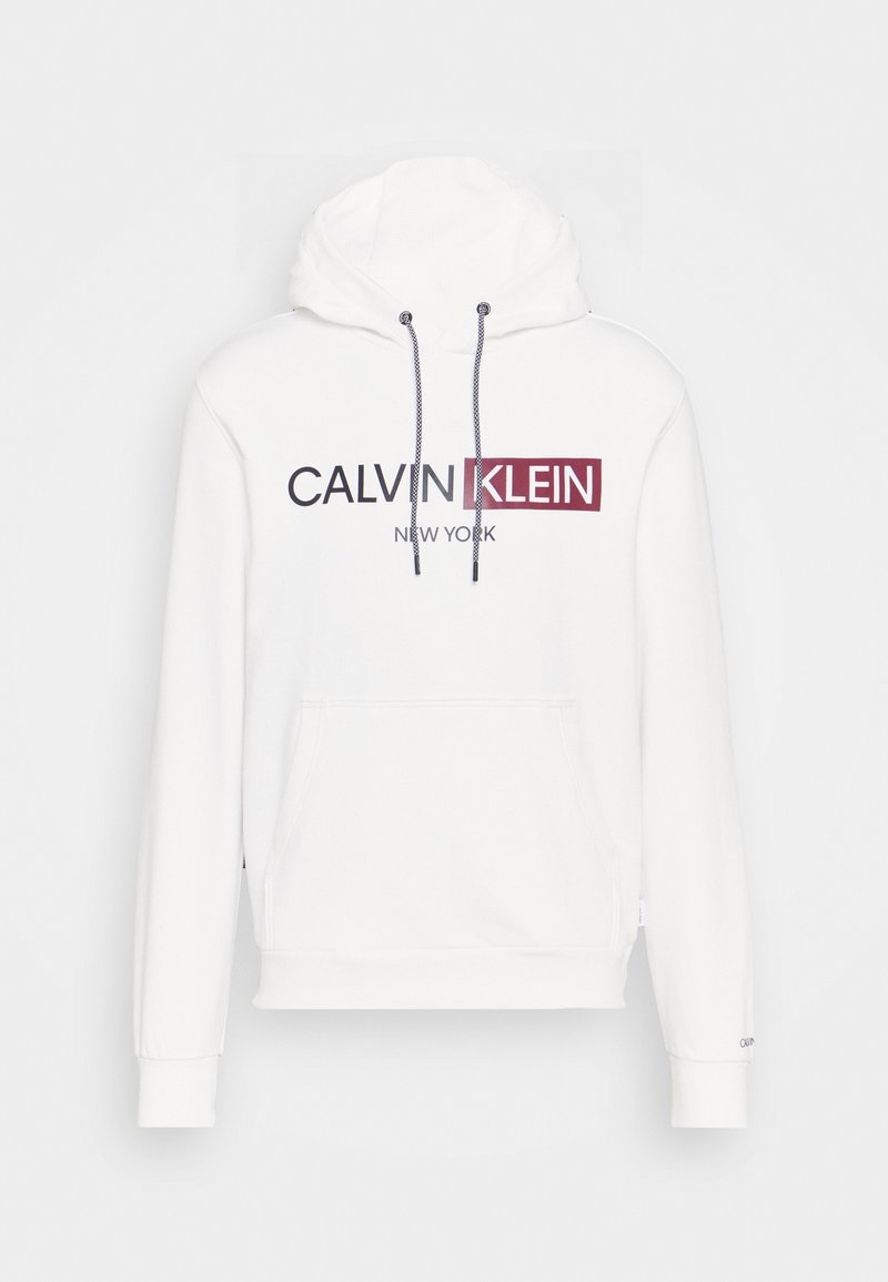 Sweat à capuche blanc avec poche kangourou à l'avant, cordons noir et blanc, et logo texte "CALVIN KLEIN NEW YORK" en noir et rouge.