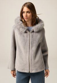 Chaqueta de piel sintética gris con una gran capucha, cierre de cremallera y mangas amplias. Textura suave y apariencia blanda, adecuada para superposiciones en clima frío.