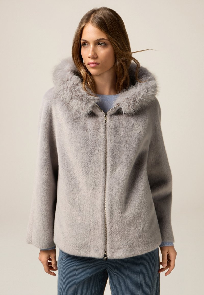 Chaqueta de piel sintética gris con una gran capucha, cierre de cremallera y mangas amplias. Textura suave y apariencia blanda, adecuada para superposiciones en clima frío.