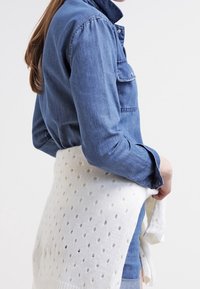 Jeansskjorta med långa ärmar, som är kombinerad med en vit stickad sjal med öppna prickmönster. Sjalet är knutet i midjan.