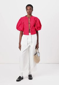 Giacca cropped rossa con maniche a sbuffo e chiusura a gancio, abbinata a pantaloni bianchi larghi e mocassini neri. Presenta una borsa tessuta testurizzata.