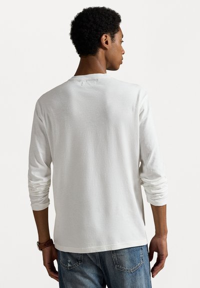 Λευκό T-shirt με μακριά μανίκια, κατασκευασμένο από βαμβάκι, διαθέτοντας χαλαρή εφαρμογή και στρογγυλή λαιμόκοψη. Η πλάτη είναι απλή με γυρισμένα μανίκια και λεία υφή.