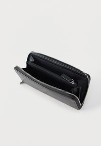 Μαύρο πορτοφόλι από δέρμα με φερμουάρ περιμετρικά, ανοιχτό για να εμφανίζει πολλαπλές θήκες για κάρτες και κεντρική θήκη για κέρματα με φερμουάρ, σε λευκό φόντο.