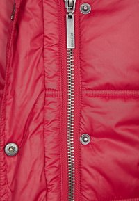 Chaqueta acolchada roja con cierre de cremallera plateada y botones de presión, con una textura suave y brillante y un detalle de acolchado.