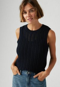 Navy stickad ärmlös topp med ett strukturerat mönster med vertikala linjer och öppna sömmar. Rund halsringning och ribbstickad fåll.