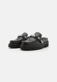 Pantofi negri din piele, slip-on, cu o talpă masivă, având accente din metal argintiu și cusături decorative pe margini.