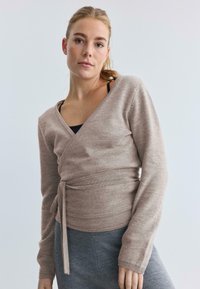 Suéter envolvente beige de manga larga, hecho de un material de punto suave. Presenta un cierre con lazo en la cintura y un diseño de escote en V.