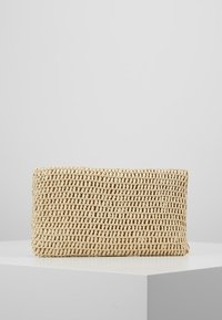 Prostokątna beżowa torebka typu clutch z plecionki, wystawiona na białym podium na jednolitym szarym tle.