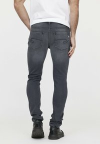 Schmale graue Jeans mit Gesäßtaschen, die über dekorative Nähte verfügen. Das Material wirkt wie Denim, und das Design ist schlicht und modern.