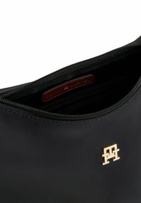 Borsa nera in nylon con chiusura zip, texture liscia, logo in hardware dorato e etichetta in pelle marrone all'interno.
