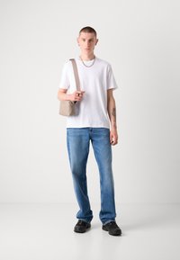 T-shirt en coton blanc, jeans en denim bleu. Sac à main marron, chaussures noires. Design simple, coupe décontractée et couleurs neutres.
