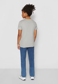 Camiseta corta gris de manga corta con cuello redondo, combinada con jeans azul rectos y zapatillas blancas. Textura suave; ajuste casual.