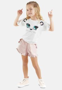 Camisa blanca de manga corta con un gráfico de cara de león y ojos azules. Pantalones cortos de satén rosa con dobladillo volado y zapatillas a juego.