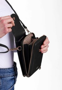 Černá kožená crossbody taška se zlatými kovovými detaily, zdobená zipovým uzávěrem, několika přihrádkami a tečkovanou textilní podšívkou.