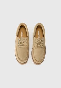 Zapatos de gamuza beige con cierre de cordones, puntera redonda, costuras de contraste y suela de goma texturizada. Nombre de la marca visible en la plantilla.