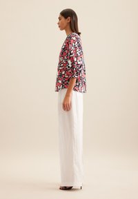 Wielokolorowa bluzka z bufkami, z kwiatowym wzorem w odcieniach różu, czerni i niebieskiego, zestawiona z białymi, szerokimi spodniami.