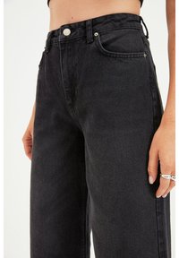 Jean noir en denim taille haute avec une coupe droite, doté de poches avant, d'un bouton en métal et d'une texture subtile.