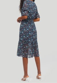 Kwiecista sukienka midi w kolorze granatowym z krótkimi bufiastymi rękawami, zwężoną talią oraz przezroczystą, zwiewną spódnicą z falbanką na dole. Białe sandały na obcasie.