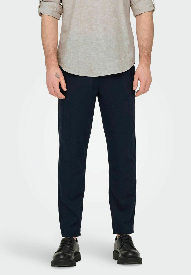 Pantaloni blu navy realizzati in tessuto leggero, con una vestibilità dritta, un leggero lucido e tasche laterali. Indossati con una camicia di colore chiaro.