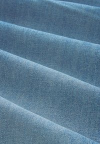 Tela de mezclilla azul claro con una textura suave, que presenta un patrón de estrías diagonales y sutiles variaciones en el sombreado a través de las secciones dobladas.