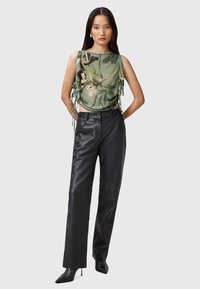 Top verde con motivo floreale, con lati drappeggiati e cordini; abbinato a pantaloni in pelle nera a vita alta e tacchi a punta.