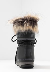 Svart vinterkänga med tan- och svart konstpälsdetalj, grå sula och "Moon Boot"-logotyp på baksidan, fotograferad mot en vit bakgrund.