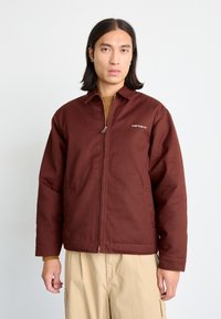 Brun zip-up jacka med solid design, krage och två framfickor. Materialet verkar hållbart med en matt finish.