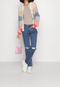 Barevný pletený svetr se pruhovanými vzory, béžový top, roztrhané modré džíny, bílé chunky tenisky a rů�žová kostkovaná kabelka.