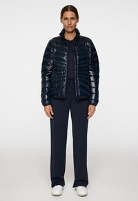 Granatowa kurtka puchowa z błyszczącym wykończeniem, pikowany wzór, wysoka stójka, noszona na dopasowanym komplecie termicznym i białych sneakersach.