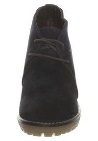 Granatowy zamszowy botek do kostki o uporządkowanym kształcie, zaokrąglonym nosku i brązowej gumowej podeszwie. Posiada płaskie sznurowadła oraz subtelne przeszycia.