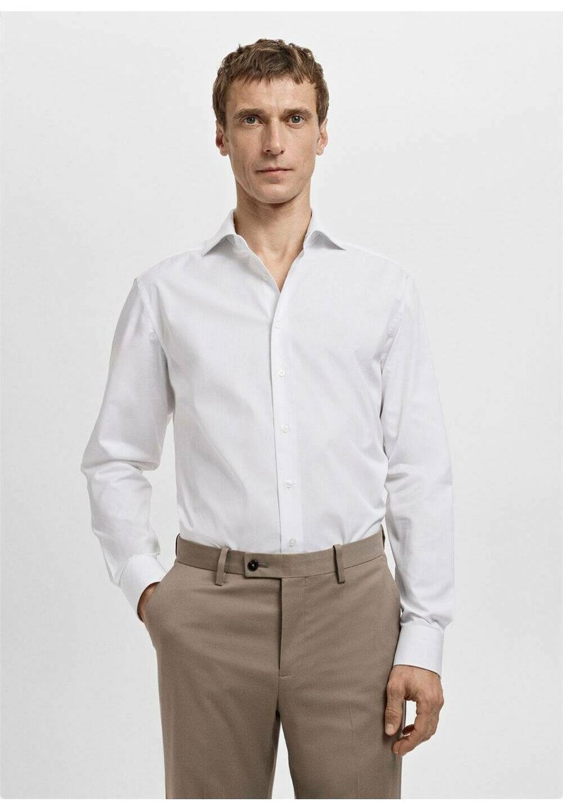 Biała koszula na guziki z kołnierzem typu włoskiego, długimi rękawami i gładką fakturą, zestawiona z beżowymi spodniami zapinanymi na guzik.