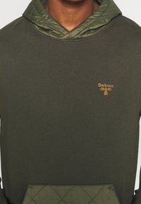 Sweat à capuche vert foncé avec capuche matelassée vert olive et poche, logo Barbour brodé en jaune sur la poitrine.