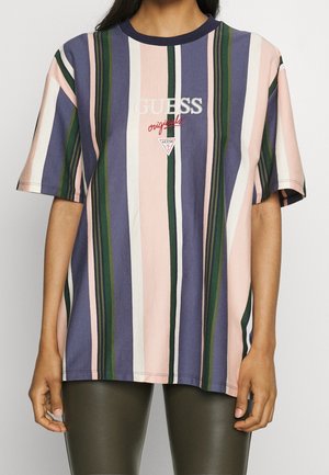 Person trägt ein locker sitzendes, gestreiftes T-Shirt in Lila, Pink, Grün und Weiß mit dem "GUESS originals"-Logo in der Mitte.