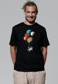 Zwarte T-shirt met een kleurrafische afbeelding van een astronaut die ballonnen vasthoudt, geïllustreerd als planeten. Korte mouwen en ronde halslijn.