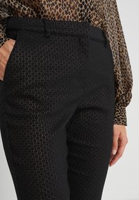 Czarne spodnie w wzór z teksturowanej tkaniny, o dopasowanym kroju oraz z paskiem w talii z zapięciem, połączone z bluzką w wzór pantery.