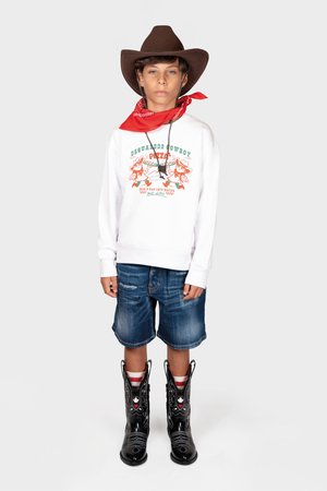 Vit sweatshirt med grafisk tryck, blå denimshorts, svarta cowboyboots med vit söm, brun hatt och röd bandana.