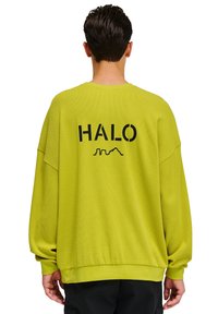 Limegrön oversized sweatshirt med ribbat mönster, med ordet "HALO" i fet svarts färg på baksidan, rund halsringning och sänkta axlar.