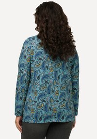 Langarmhemd in Türkis mit einem Paisleymuster, das blaue, gelbe und schwarze Akzente aufweist. Glattes Material mit einer lockeren Passform.