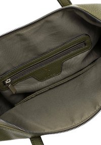 Intérieur d'un sac à main en cuir vert, comprenant une poche zippée, une doublure en tissu lisse et un logo délicatement embossé. Fermeture zippée sur le dessus.