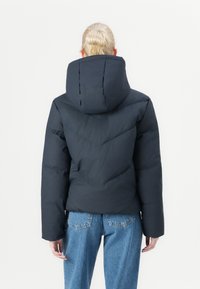 Dark navy puffer jacket with a large hood, featuring a quilted pattern and wide sleeves. Paired with high-waisted light blue jeans.