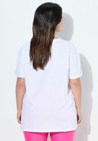 Camiseta blanca de algodón con un corte relajado, escote redondo y mangas cortas, combinada con leggings de un rosa brillante, vista desde la espalda.