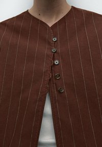 Brun knap-i-ned beklædning med lodrette hvide striber, med V-udskæring og fem dekorative knapper foran.