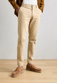 Khaki chino's met een standaard pasvorm, glad katoenmateriaal, zijzakken, afgewerkt met brown suède instapschoenen en gestructureerde zolen.