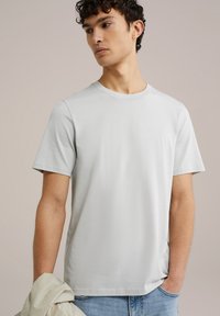 Šviesiai pilkas trumpomis rankovėmis marškinėliai, su apvalia iškirpte, pagaminti iš lygaus medvilninio audinio, pasižymintys laisvu siluetu ir paprastu dizainu, dėvimi su šviesiais džinsais.